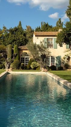 a pool in front of a house with trees and bushes around the edge, surrounded by greenery