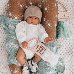 a baby laying on top of a blanket wearing a white sweater and knitted hat