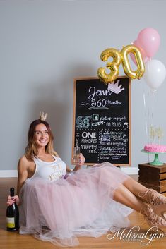 a woman sitting on the floor in front of a chalkboard with balloons and a wine bottle