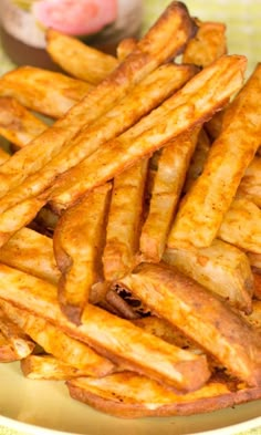 some french fries are on a plate and ready to be eaten with dipping sauce in the background