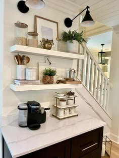 a kitchen counter with coffee maker, cups and other items on the shelves above it