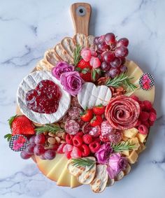 a platter filled with fruit and cheese on top of a marble countertop next to a cutting board