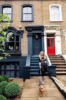 a woman is walking her dog in front of a brick building with blue doors and windows