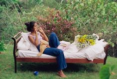 a woman sitting on top of a bed in the grass next to flowers and plants