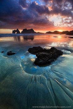 the sun is setting over some rocks in the water