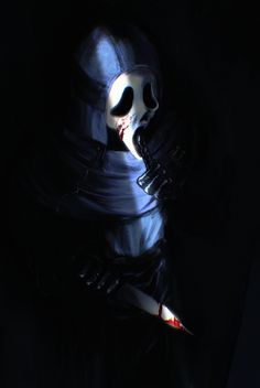 a person wearing a mask and holding a knife in the dark with their face painted white