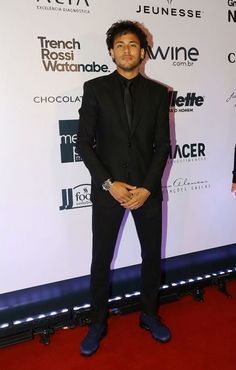 a man in a suit and tie standing on a red carpet with his hands in his pockets