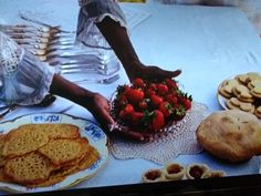 a person reaching for some food on a table with cookies and strawberries in front of them