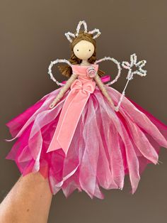 a hand is holding a doll with pink tulle