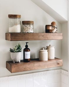 two wooden shelves with bottles and soaps on them in a white tiled bathroom under a slanted ceiling