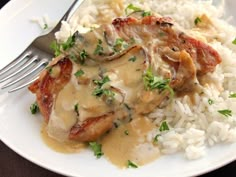 a white plate topped with meat covered in gravy next to rice and a fork