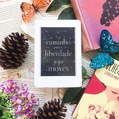 a tablet sitting on top of an open book next to some flowers and pine cones