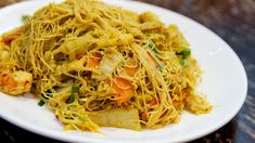 a white plate topped with noodles and vegetables on top of a wooden table next to a fork