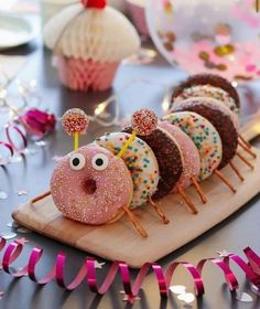 there are donuts with sprinkles and eyes on the wooden board next to pink streamers