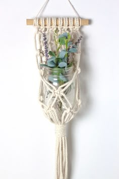 a macrame wall hanging with flowers and mason jars on the top, attached to a rope