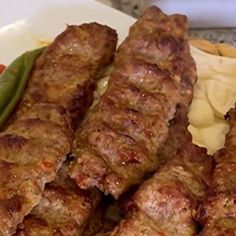 several skewers of meat sitting on top of a plate next to some vegetables