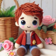 a small crocheted boy sitting next to some flowers and baskets on a table