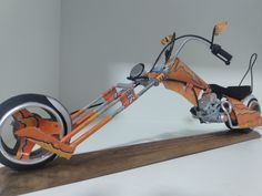 an orange and black scooter is on a wooden stand with white walls in the background