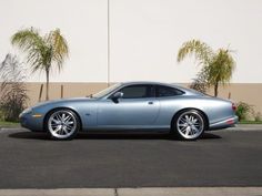 a blue sports car is parked in front of a building with palm trees behind it