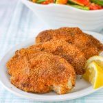 two chicken patties on a white plate with a side salad