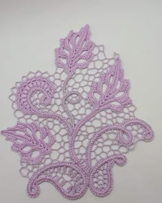 a crocheted doily is shown on a white tablecloth with purple flowers and leaves