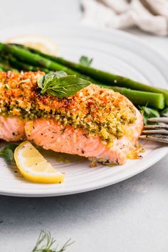 salmon and asparagus on a white plate with lemon wedges next to it