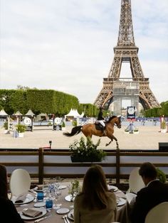 a horse jumping over a table in front of the eiffel tower with people sitting around it