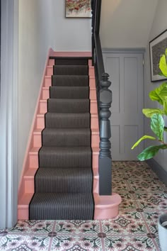 a pink and black stair case next to a potted plant on the side of a staircase