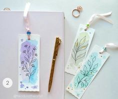 three bookmarks with watercolor designs on them next to a pen and some scissors