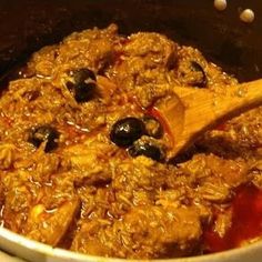 meat and olives are being cooked in the slow cooker with a wooden spoon