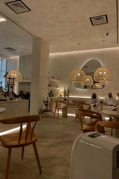 an empty restaurant with wooden chairs and round lights hanging from the ceiling, along with people sitting at tables