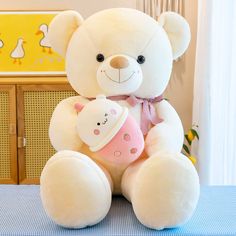 a large white teddy bear holding a pink cup on top of a blue table cloth