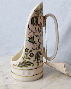 a ceramic coffee cup shaped like a boat with flowers painted on the side and gold trimmings