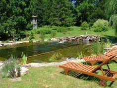 two wooden picnic tables sitting next to a river in a park area with grass and trees