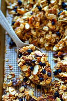 a wooden spoon filled with granola on top of a baking sheet covered in nuts and raisins