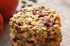 three granola bars stacked on top of each other with fruit and nuts in the background