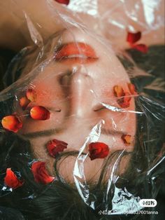 a woman laying on top of a plastic bag covered in rose petale petals with her eyes closed