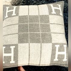 a person holding a gray and white pillow with the letter h on it's side