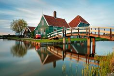 a wooden bridge crossing over a body of water next to green houses with red roofs