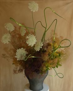 a vase filled with lots of flowers on top of a white table next to a wall