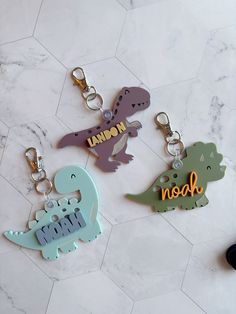 three dinosaur key chains with the word mom written on them sitting on a marble surface