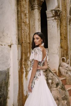 a woman standing in front of an old building wearing a dress with flowers on it