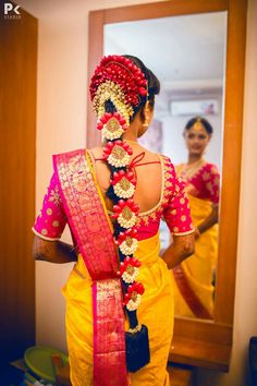 a woman wearing a yellow sari with red and gold jewelry on her neck, standing in front of a mirror