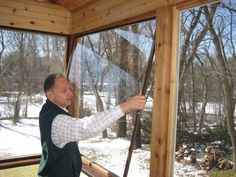 a man standing in front of a window looking out at the snow covered trees outside