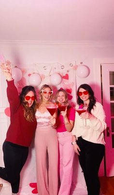 four women pose for a photo in front of balloons and heart - shaped glasses at a valentine's day party