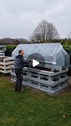 a man standing in front of a greenhouse with plants growing out of the top and bottom