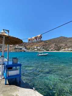 there are two chairs and an umbrella on the water near some boats in the ocean