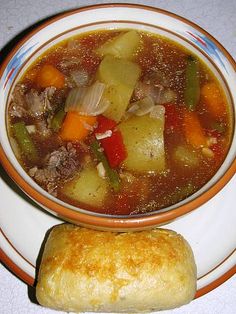 a bowl of soup next to a roll on a plate