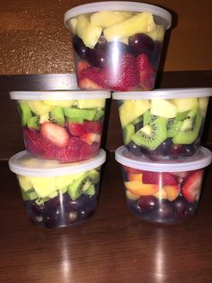 four plastic containers filled with fruit sitting on top of a wooden table next to a wall