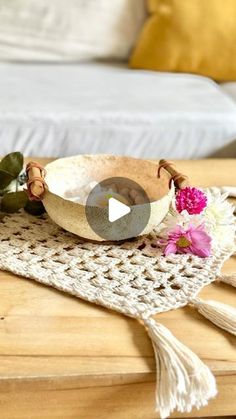 a wooden table topped with a bowl filled with flowers and greenery next to a bed